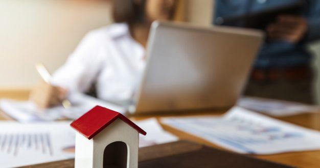 Business people are discussing about the real estate project behind home architectural model. The couple was consulting before buying the house. Real estate business concept.