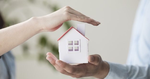 close-up-hands-protecting-small-house-model_23-2148204008