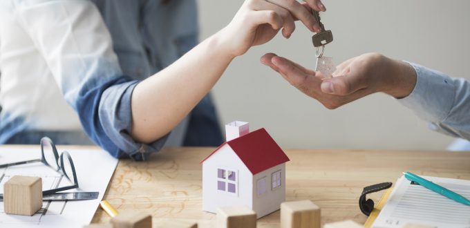 close-up-of-woman-s-hand-giving-house-key-to-man-over-wooden-table