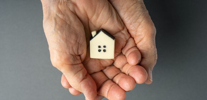 Inheritance concept. Elderly woman hands holds a little toy house. Inherited property idea.