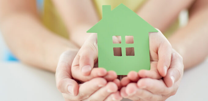 people, charity, family and home concept - close up of woman and girl holding green paper house cutout in cupped hands